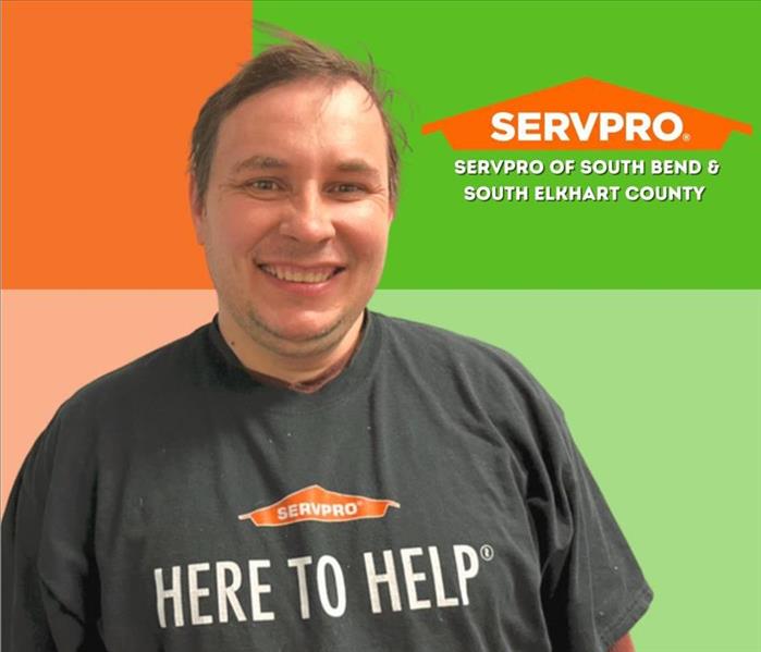 man wearing a SERVPRO shirt smiles at camera with a multi colored background and a SERVPRO logo behind him